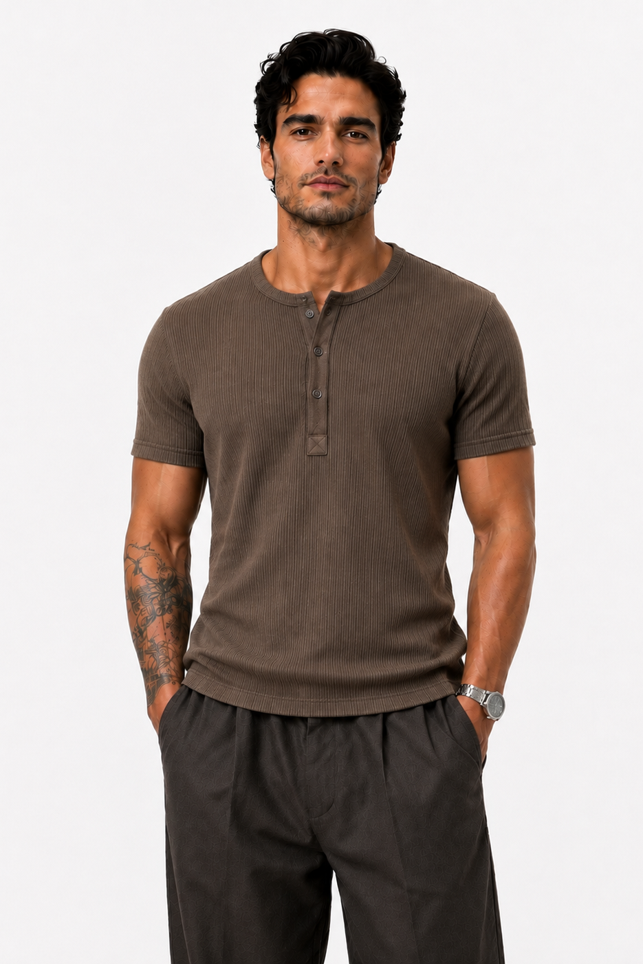 A man modeling a short-sleeve henley shirt in a dark brown color, paired with dark gray pants, against a plain light gray background.