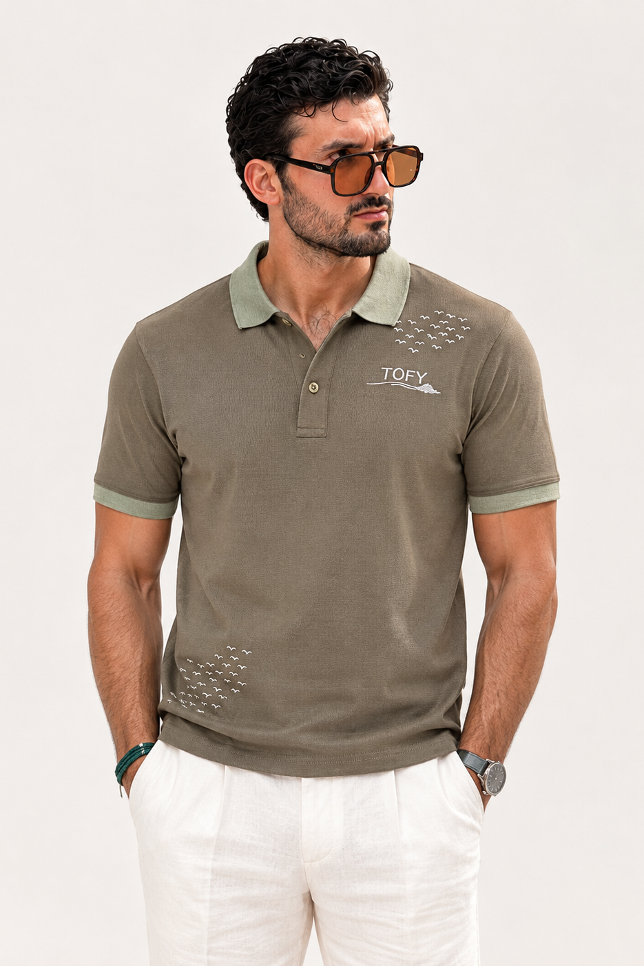 A man wearing a TOFY short-sleeve polo shirt in olive green with matching green collar and sleeve cuffs, paired with white trousers, against a plain light background.