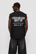 A man viewed from the back wearing a black sleeveless t-shirt with bold white text on the back, paired with baggy black jeans and black-and-white sneakers, against a light gray studio background.