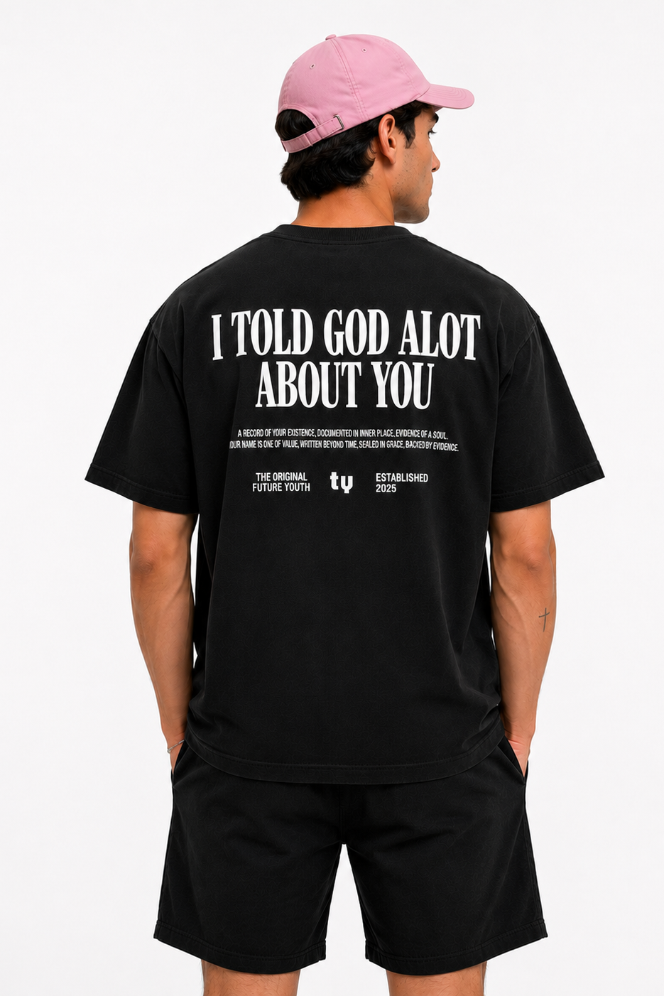 A man wearing a black t-shirt and shorts, viewed from the back. The t-shirt features a large white graphic text on the back reading 'I TOLD GOD ALOT ABOUT YOU' with smaller text below.